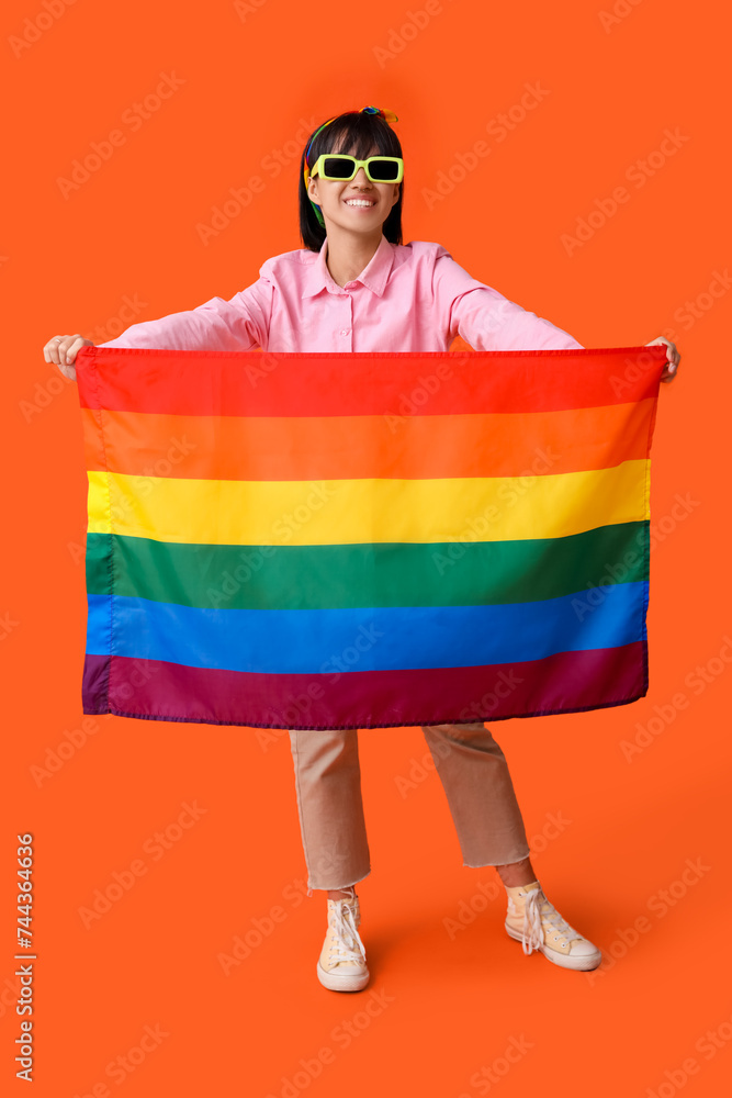 Beautiful young woman with LGBT flag on orange background