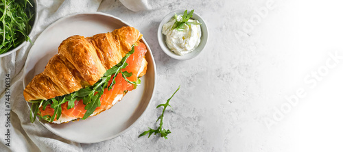 croissant sandwich, healthy breakfast. top view shot of Croissant sandwich with cream cheese, salmon and arugula on a white plate, copy space