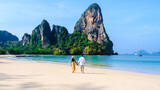 a couple of men and women relaxing on the beach during a vacation in Thailand Railay Beach Krabi with beautiful limestone cliffs in the background