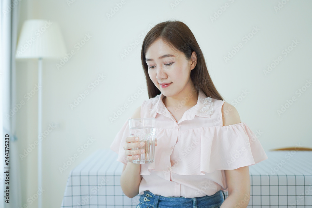 Cheerful Asian young woman drinking a water in a glass close up with copyspace. Asian working woman holding a glass of drinking water and smiling to camera. Work life balance concept. Cheerful Asian young woman drinking a water in a glass close up with copyspace. Asian working woman holding a glass of drinking water and smiling to camera. Work life balance concept.