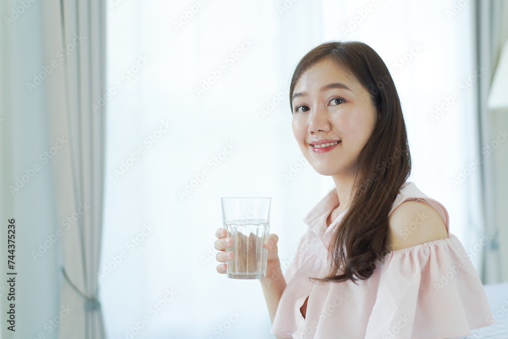 Cheerful Asian young woman drinking a water in a glass close up with copyspace. Asian working woman holding a glass of drinking water and smiling to camera. Work life balance concept. Cheerful Asian young woman drinking a water in a glass close up with copyspace. Asian working woman holding a glass of drinking water and smiling to camera. Work life balance concept.