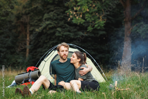 Young couple sitting near fire near tent in forest at summer