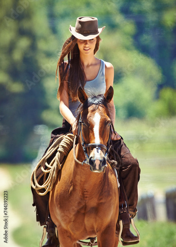 Woman, cowgirl and horse riding in the countryside for journey, travel or outdoor adventure in nature. Female person or western rider with hat, saddle and animal stallion at ranch, farm or stable © Y.A./peopleimages.com