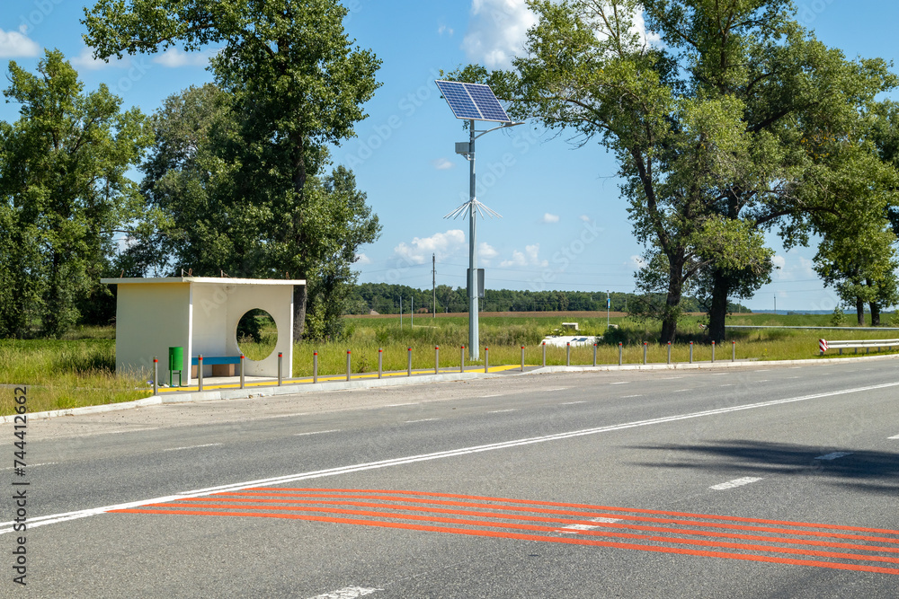 Fototapeta premium Lamp post with solar panel system on road with blue sky and trees. Autonomous street lighting using solar panels. Street lamp, on batteries from the sun. Alternative renewable energy systems