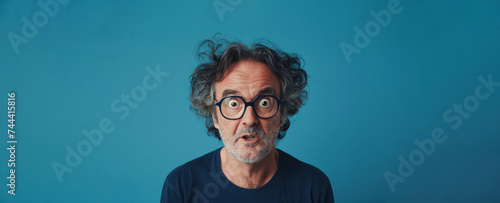 surprised mature man with glasses and voluminous hairstyle on a blue background. face of surprise and curiosity.blue background . copy space for advertising  presentations or promotional banners