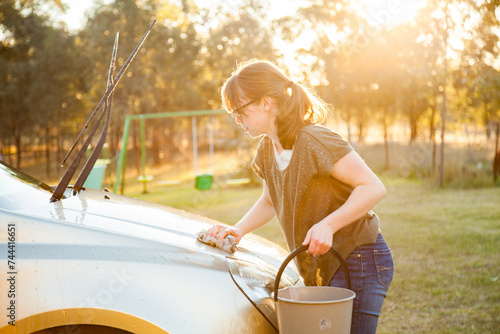 Teen girl washing family car in natural afternoon sunlight photo