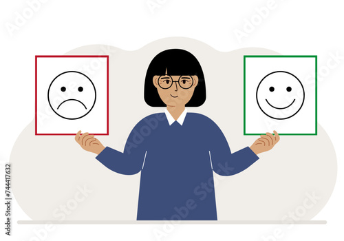 Smiling woman holds a card with a sad emoji in one hand and a smiling emoji in the other hand. The concept of emotions, masks or psychological help.