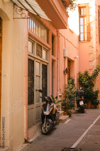 Motorbikes parked by pink building in an alleyway in Crete, Greece