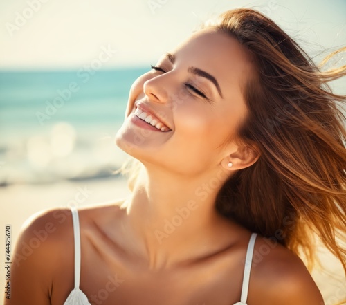 a woman with long hair smiling at the camera on a beach with the sun shining on her face 