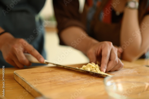 Man chopping garlic on wooden board, young couple preparing meal in the kitchen