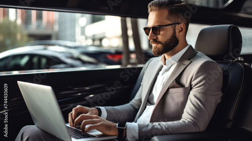 A handsome executive uses his laptop while enjoying the comfort of a luxury car. photo