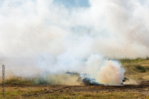 Heavy combat vehicles tanks drive around the butts and put up a smoke screen