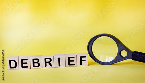 Wooden cubes with debrief text on a yellow background next to a magnifying glass photo