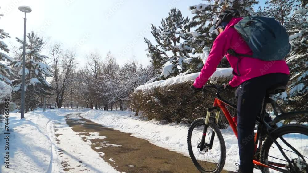 A girl in a pink jacket rides a bicycle along a path in the park after a snowfall. Winter cycling adventure. Active lifestyle. Slow motion A girl in a pink jacket rides a bicycle along a path in the park after a snowfall. Winter cycling adventure. Active lifestyle. Slow motion