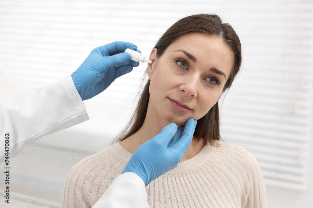 Doctor applying medical drops into woman's ear indoors Doctor applying medical drops into woman's ear indoors