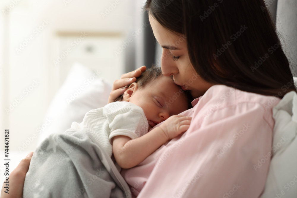 Mother kissing her sleeping newborn baby in bed at home Mother kissing her sleeping newborn baby in bed at home