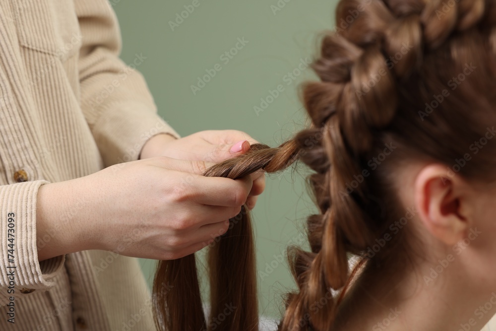 Professional stylist braiding woman's hair on olive background, closeup Professional stylist braiding woman's hair on olive background, closeup