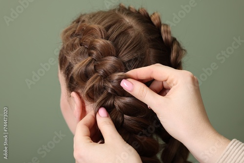 Professional stylist braiding woman's hair on olive background, closeup