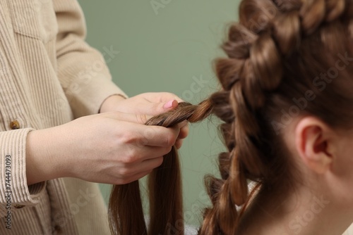 Professional stylist braiding woman's hair on olive background, closeup