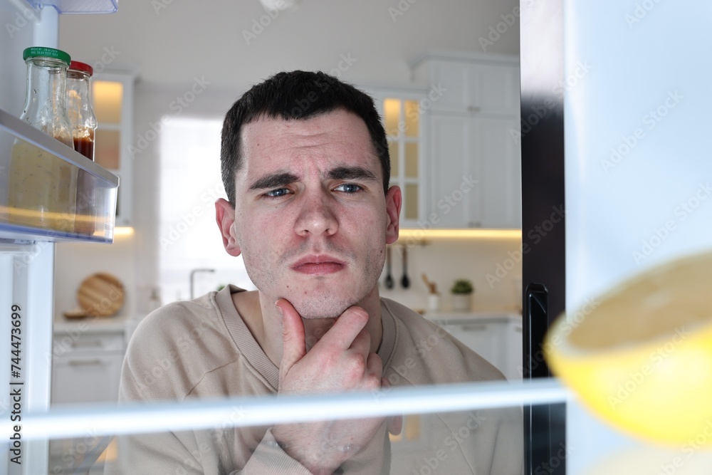 Upset man near empty refrigerator in kitchen, view from inside