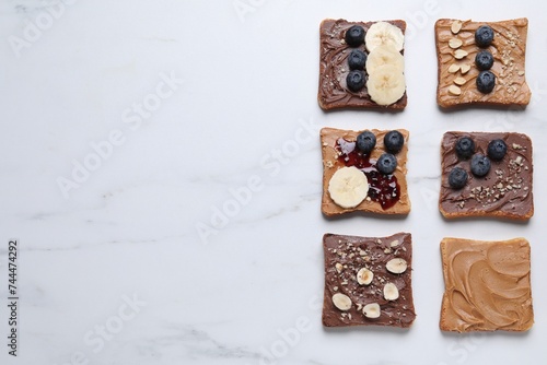 Different tasty toasts with nut butter and products on white marble table, flat lay. Space for text