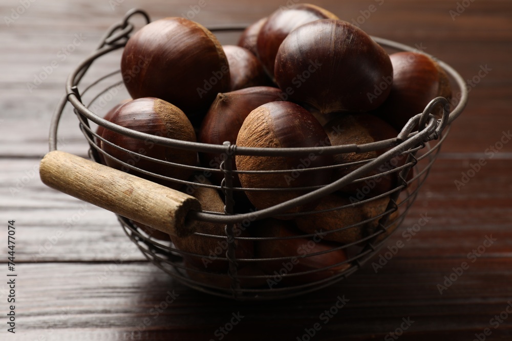 Sweet fresh edible chestnuts in metal basket on wooden table, closeup Sweet fresh edible chestnuts in metal basket on wooden table, closeup