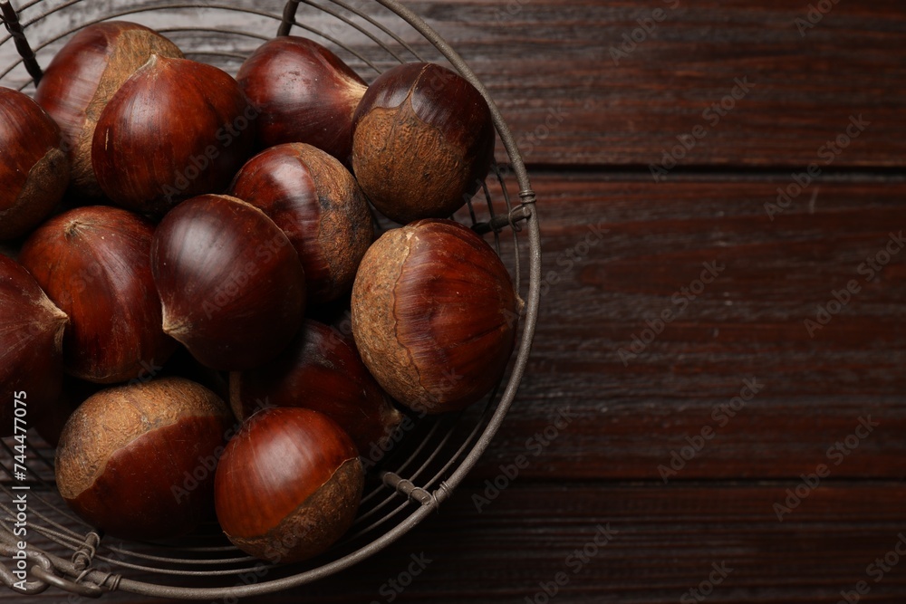 Sweet fresh edible chestnuts in metal basket on wooden table, top view. Space for text Sweet fresh edible chestnuts in metal basket on wooden table, top view. Space for text