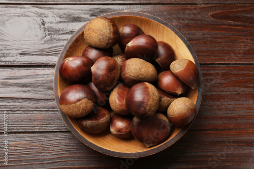 Sweet fresh edible chestnuts in bowl on wooden table, top view