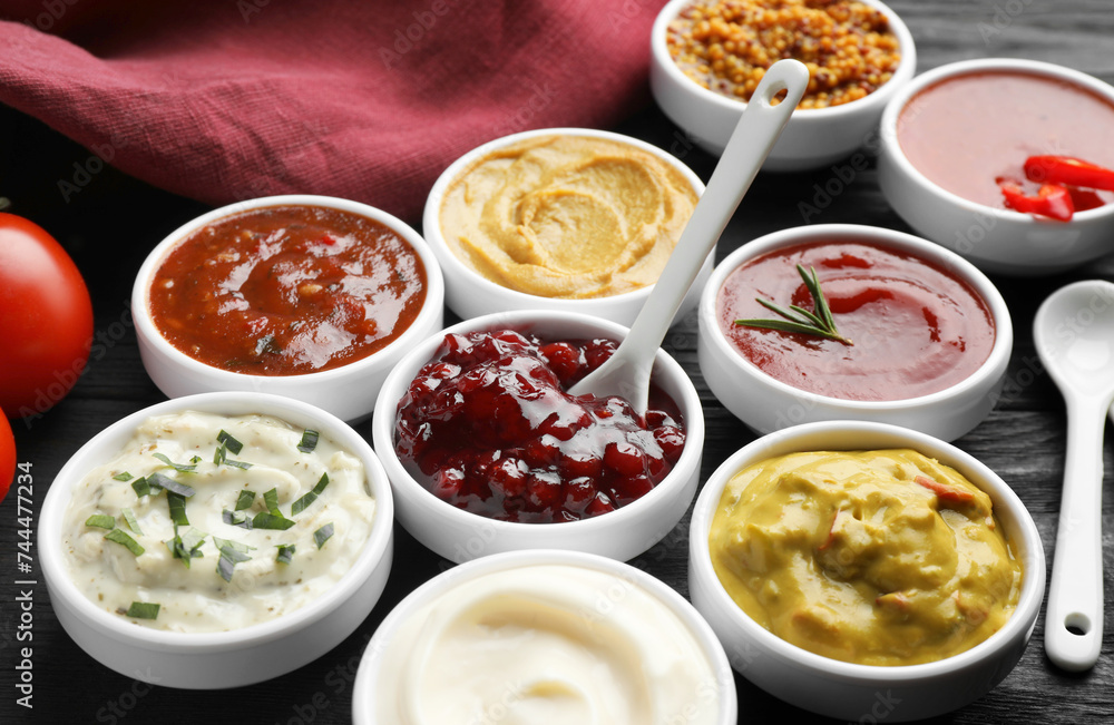 Different tasty sauces in bowls and spoons on black wooden table, closeup Different tasty sauces in bowls and spoons on black wooden table, closeup