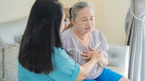 Sick older woman with chest pain touching inflammated zone and middle-aged woman or nurse take care of her. photo