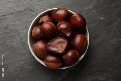 Roasted edible sweet chestnuts in bowl on grey textured table, top view