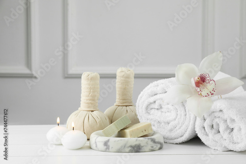 Beautiful spa composition. Towels, herbal bags, soap bars and burning candles on white wooden table, space for text