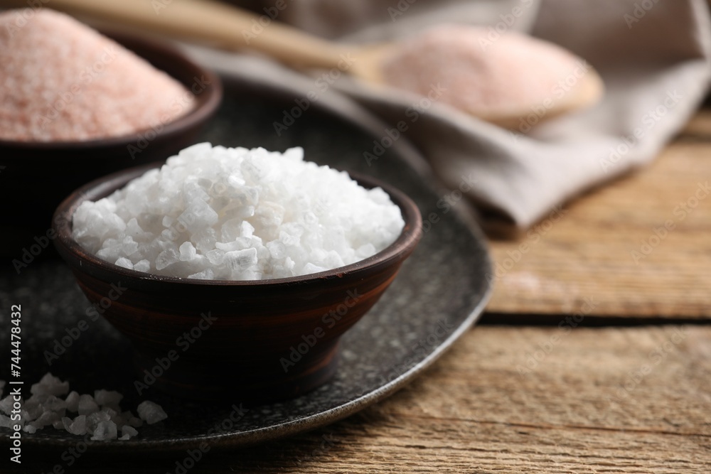Different salt in bowls on wooden table, closeup. Space for text Different salt in bowls on wooden table, closeup. Space for text