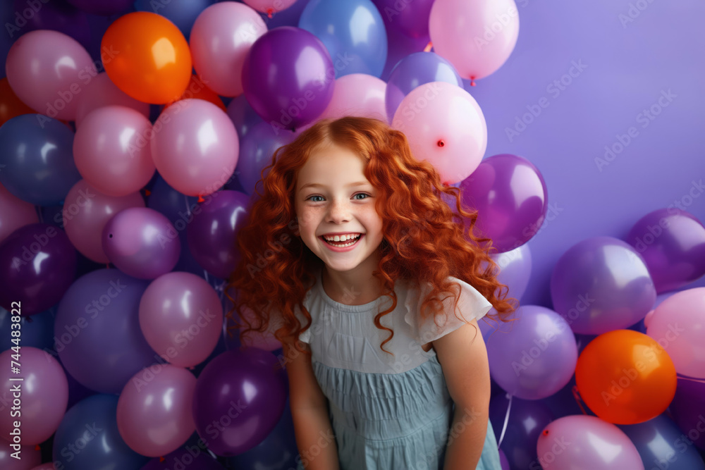 Laughing little redhead curly girl with air balloons on violet background.