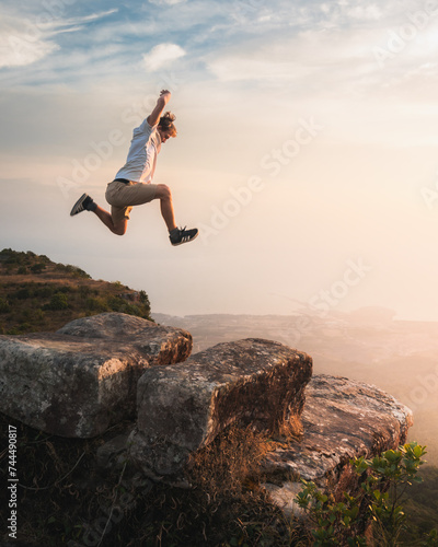 A man jumping on a rock at sunset at the top of a mountain