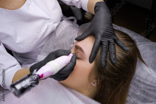 Hands of the master in black sterile gloves that perform permanent eyebrow makeup. PMU Procedure, Permanent Eyebrow Makeup. photo