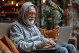 Elderly man using laptop in comfortable chair under a tree