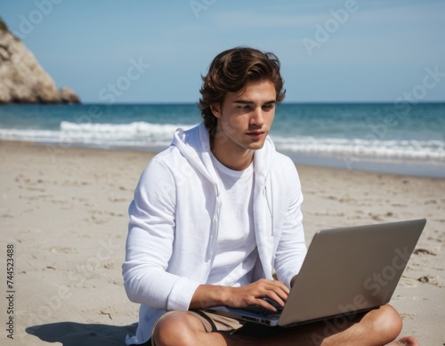 An young man sitting on a beach with laptop and working remotely © orelphoto