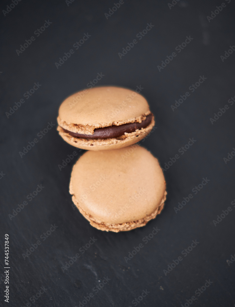 A collection of beautiful chocolate filled French macaroons sweet dessert, served on a rustic slate plate. Gourmet and posh trendy cafe and bakery treat. Sugar sweeties.