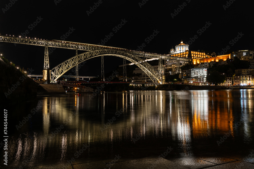 Dom Luis I bridge over Douro river and monastery of Serra do Pilar illuminated at night. Porto, Portugal. In first row some Rabelos, a type of boat traditionally used to transport wine barrels