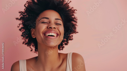 woman with curly hair is laughing joyfully against a coral pink background.