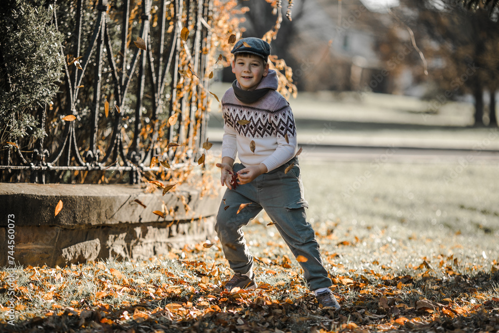 Portrait of happy cute little kid boy with autumn leaves background in colorful clothing. Funny child having fun in fall forest or park on cold day. Casual fashion for winter children clothes.