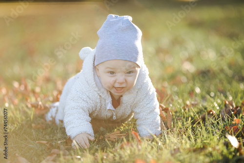 Adorable baby crawling in fallen leaves in morning sunlight.