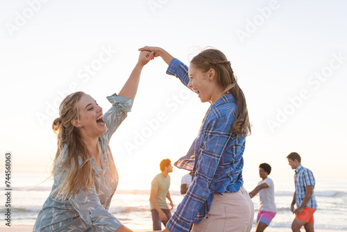 Two young Caucasian women dance on the beach at sunset
