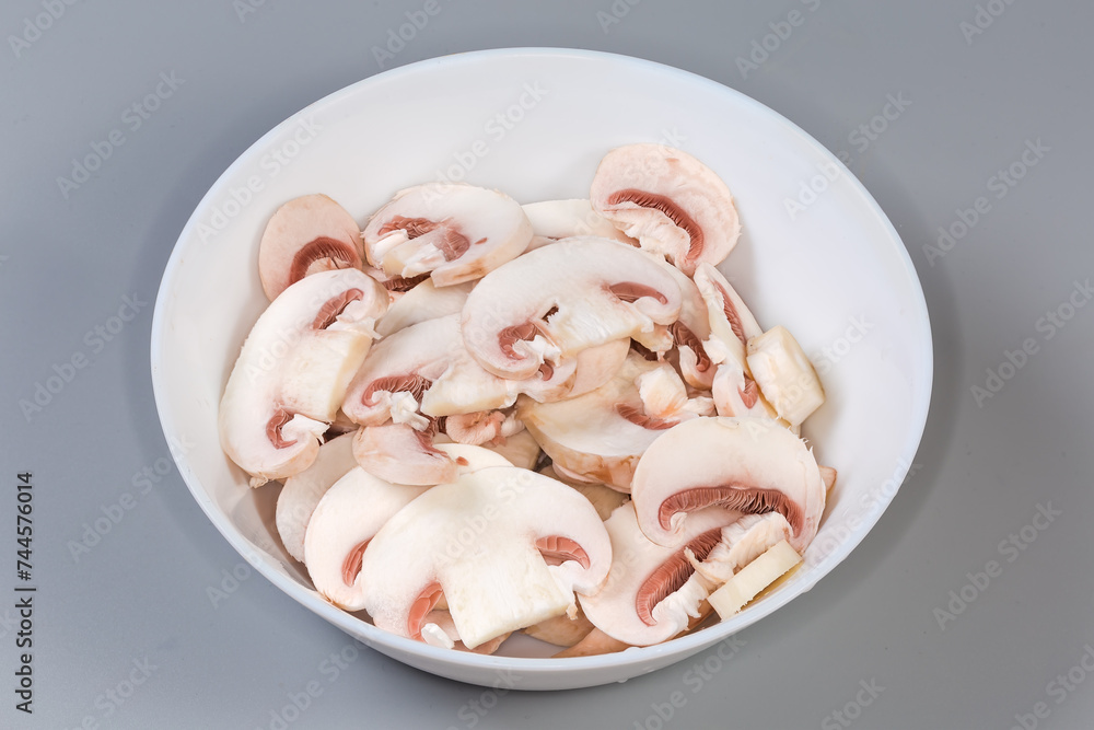 Raw sliced button mushrooms in bowl on gray background Raw sliced button mushrooms in bowl on gray background