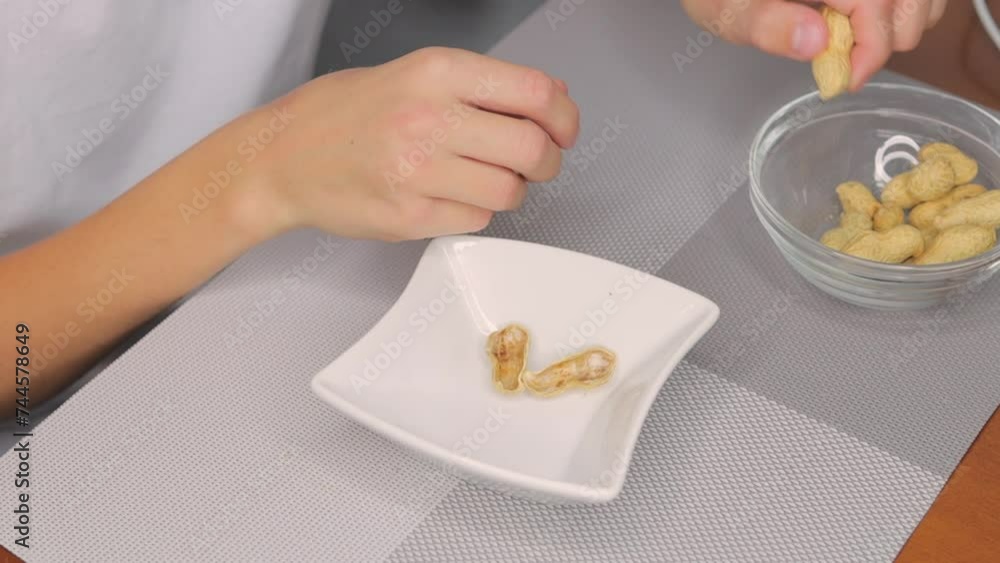 a boy in a white T-shirt sits at the table peeling and eating peanuts a boy in a white T-shirt sits at the table peeling and eating peanuts