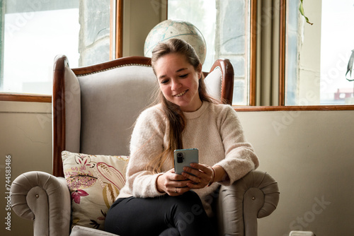 Mujer viendo su teléfono móvil sentada en el sofá de su sala de estar	 photo