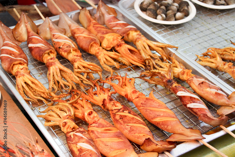 Grilled squid with sauce on skewers selling in thailand street food market with seafood