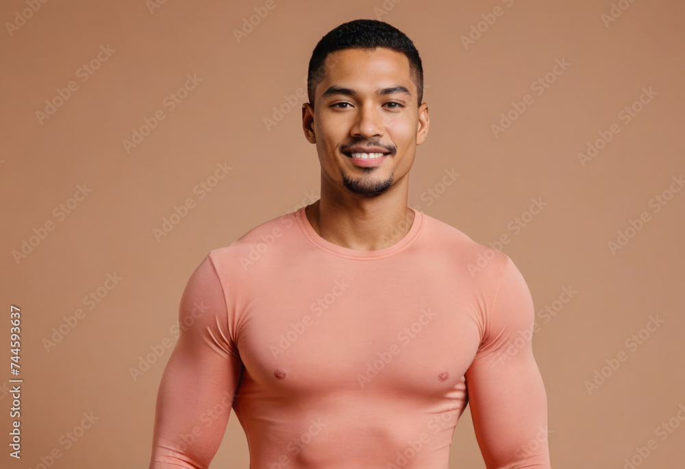 A fit man in a form-fitting peach shirt, his poise and smile suggesting confidence and a friendly demeanor.
