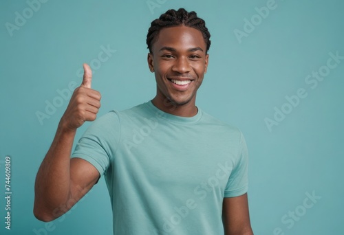 A lively young man in a teal t-shirt gives a thumbs up, his energetic demeanor and bright smile indicating joy and satisfaction.